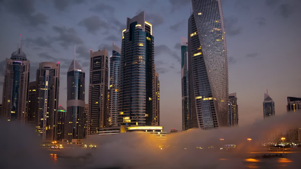 Illuminated skyscrapers of Dubai Marina rise dramatically from a dense layer of low clouds at dusk, forming a striking and futuristic cityscape that captivates with its urban elegance