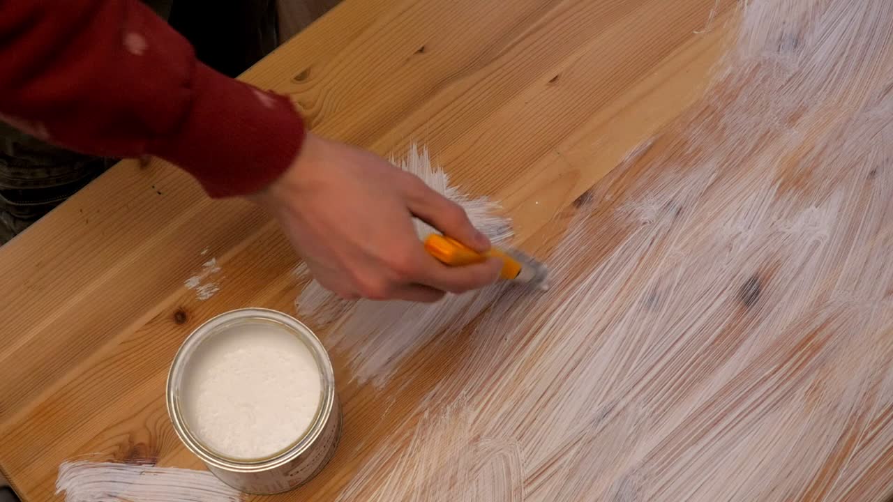 el trabajador pinta la mesa de madera con color blanco con un pincel del cubo de pintura