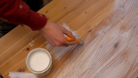 worker paints wooden table with white color with brush from the paint bucket