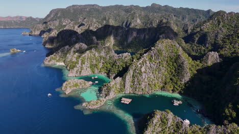 aerial drone view of coron island’s dramatic cliffs, tropical greenery, and idyllic turquoise waters. with bungalows and boats in the lagoons.