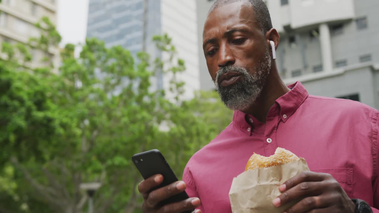 African American man eating and using his phone in the street