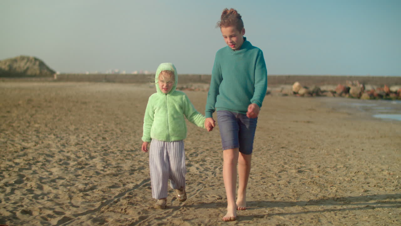 niño con la hermana menor caminando por la playa en un día fresco