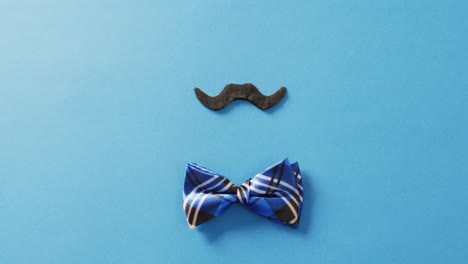 Video-of-false-moustache-with-blue-checked-bow-tie-on-blue-background-with-copy-space