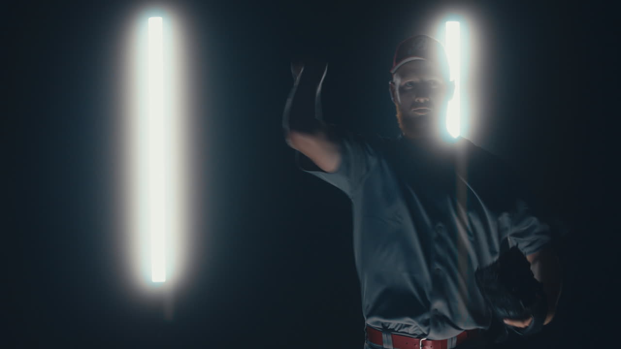 jugador de béisbol profesional caucásico lanzando una pelota hacia la cámara contra un fondo oscuro. 4k uhd 60 fps cámara lenta