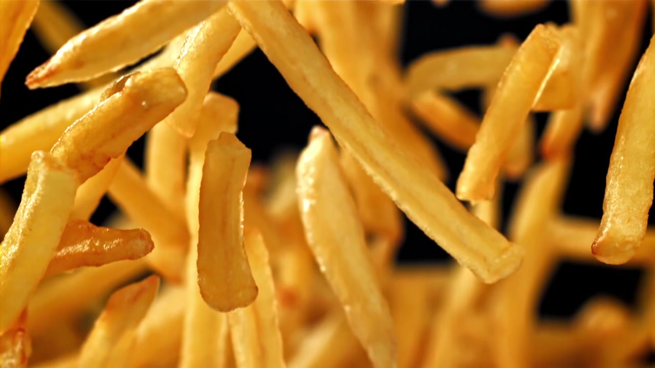 Goldene Pommes Frites fallen in Zeitlupe auf schwarzem Hintergrund.