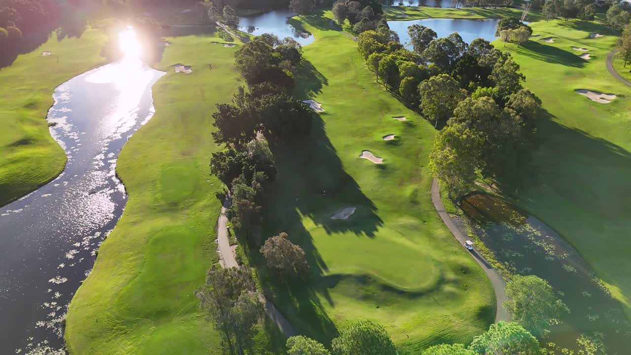 Drone captures serene golf course landscape with lush greens and water features during golden hour on the Gold Coast