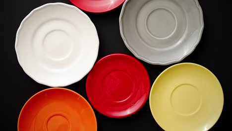 Colorful-empty-plates-and-saucers-over-black-background-