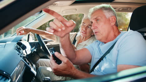 senior couple in car arguing about directions on gps sat nav on mobile phone on day trip out