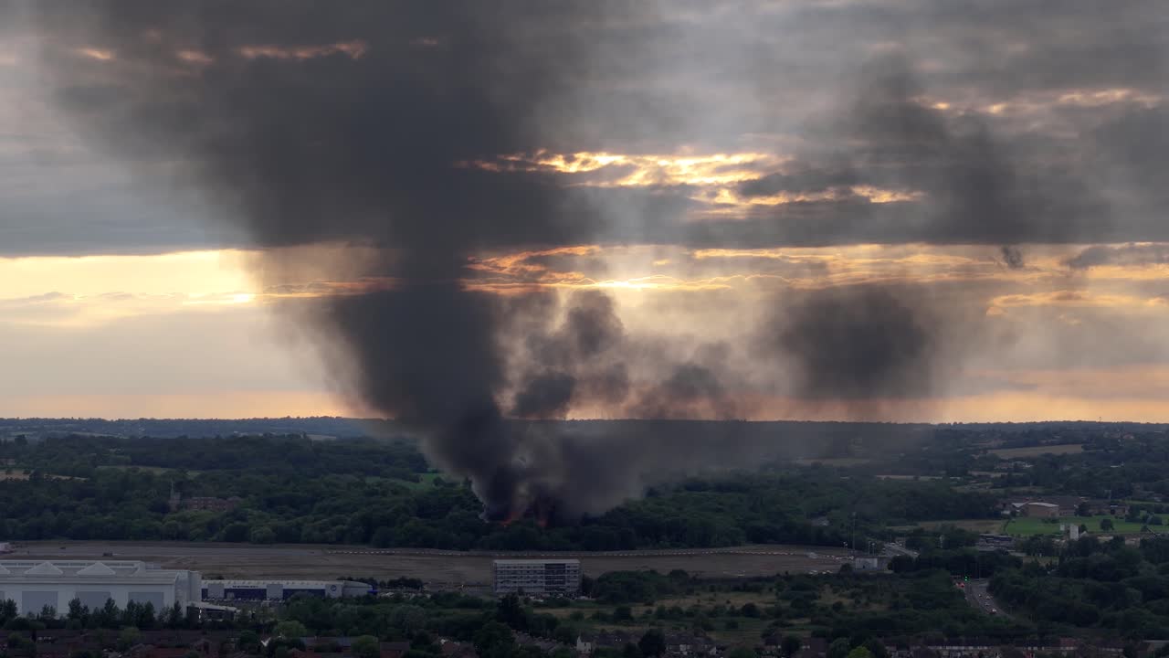 Large Plume of Black Smoke Rising from a Fire in a Forested Area at Sunset