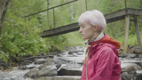 mujer de cabello rosa junto a un arroyo y un puente