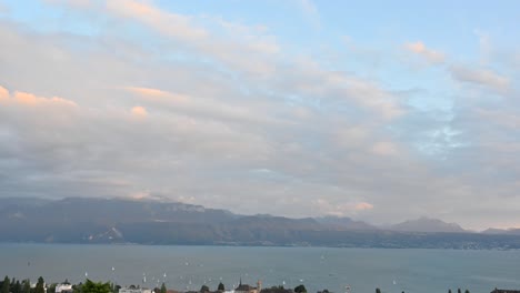 Zeitraffer-Des-Genfersees-Am-Abend:-Segelbootrennen-Nahe-Der-Schweizer-Küste,-Wolken-Ziehen-Am-Himmel,-Beleuchtet-Von-Der-Warmen-Sonnenfarbe