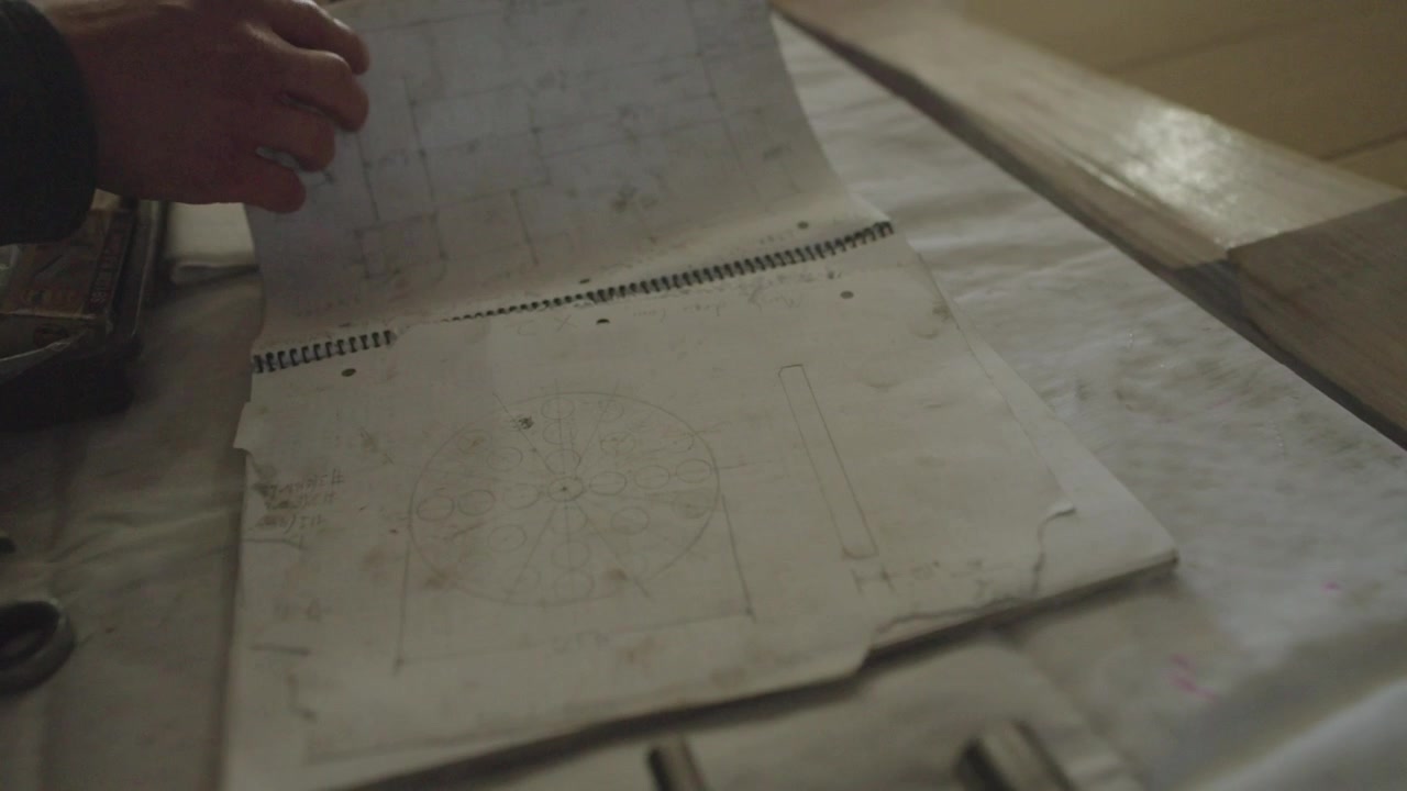 A slow motion shot of a mechanic opening an flipping through their blueprint, spec book on their workbench surrounded by tools in their workshop