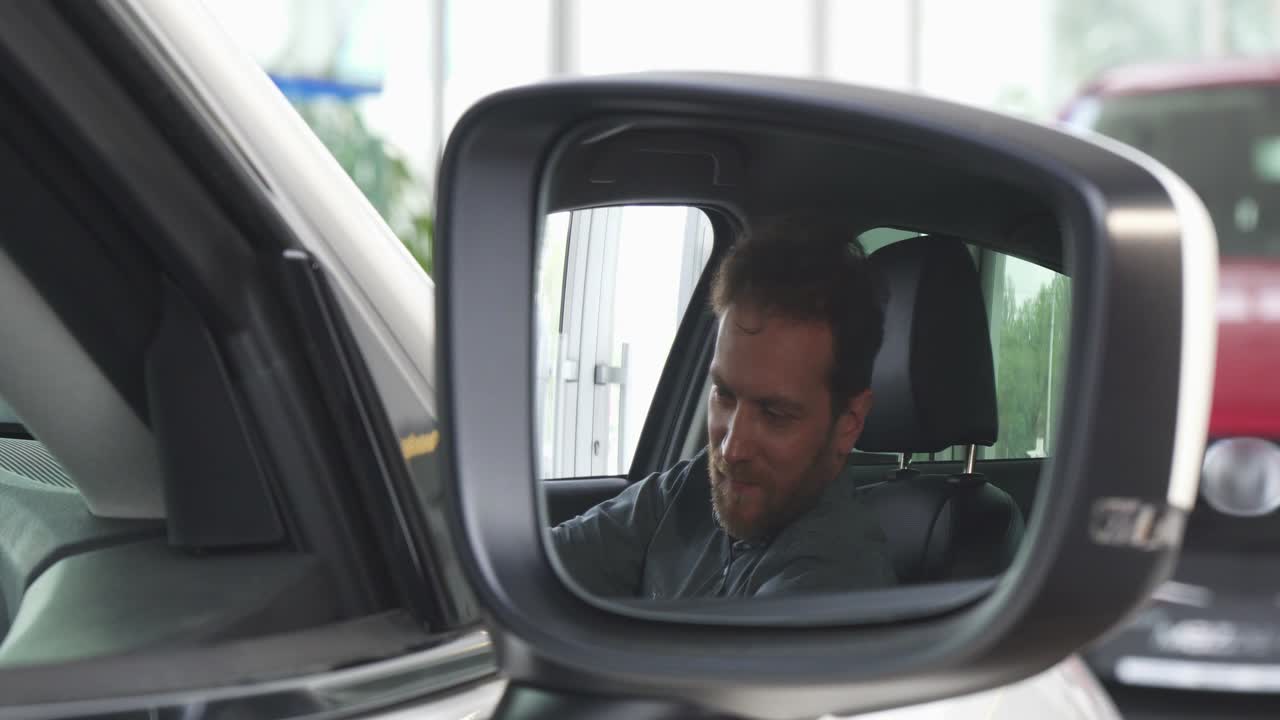 Selektivt fokus på et sidespeil på en bil, lykkelig mann slapper av i en ny bil
