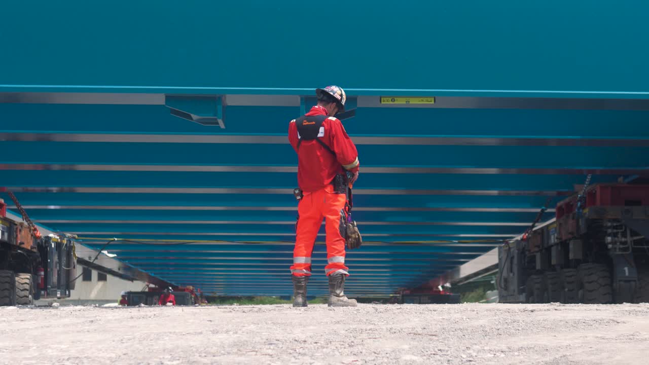 Construction worker in orange gear inspects bridge rigging under a steel structure in South France