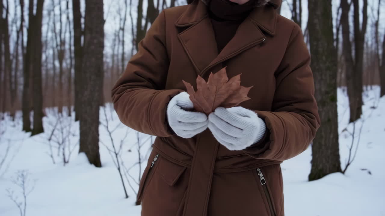 Person holding a dried leaf in a snowy winter forest