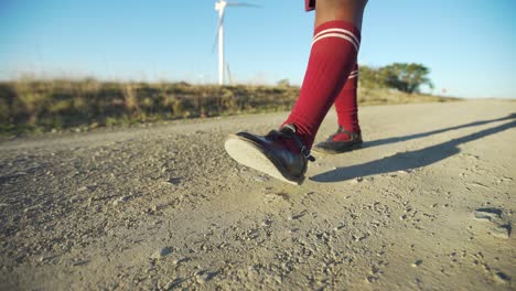 colegiala caminando por un camino de ripio junto a turbinas eólicas, ángulo bajo