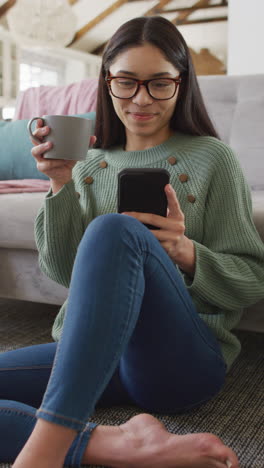 video vertical de una mujer biracial usando un teléfono inteligente y bebiendo café