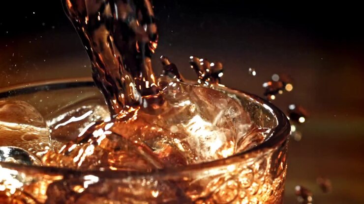 Versamento al rallentatore di una bevanda ambrata in un bicchiere con ghiaccio