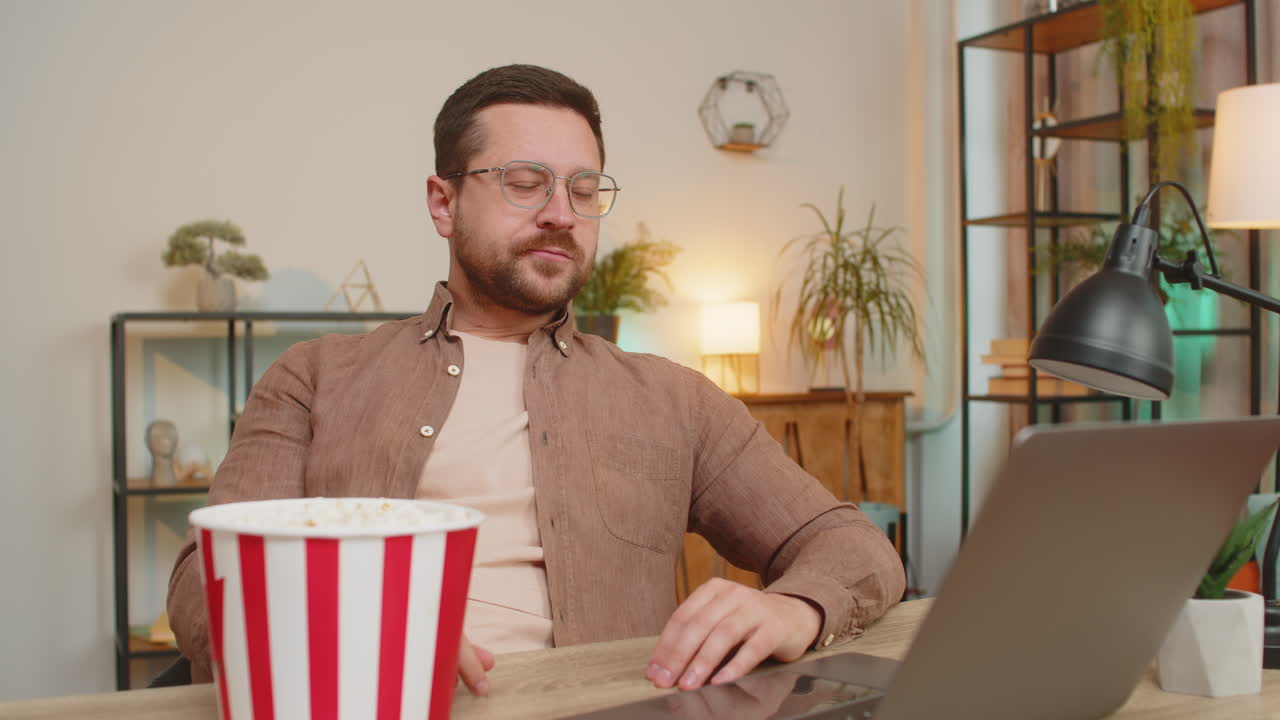 joven empresario feliz tomando un descanso del trabajo comiendo palomitas de maíz y viendo películas en la computadora portátil en casa