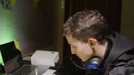 young caucasian man working on laptop, making notes on paper and typing on keyboard