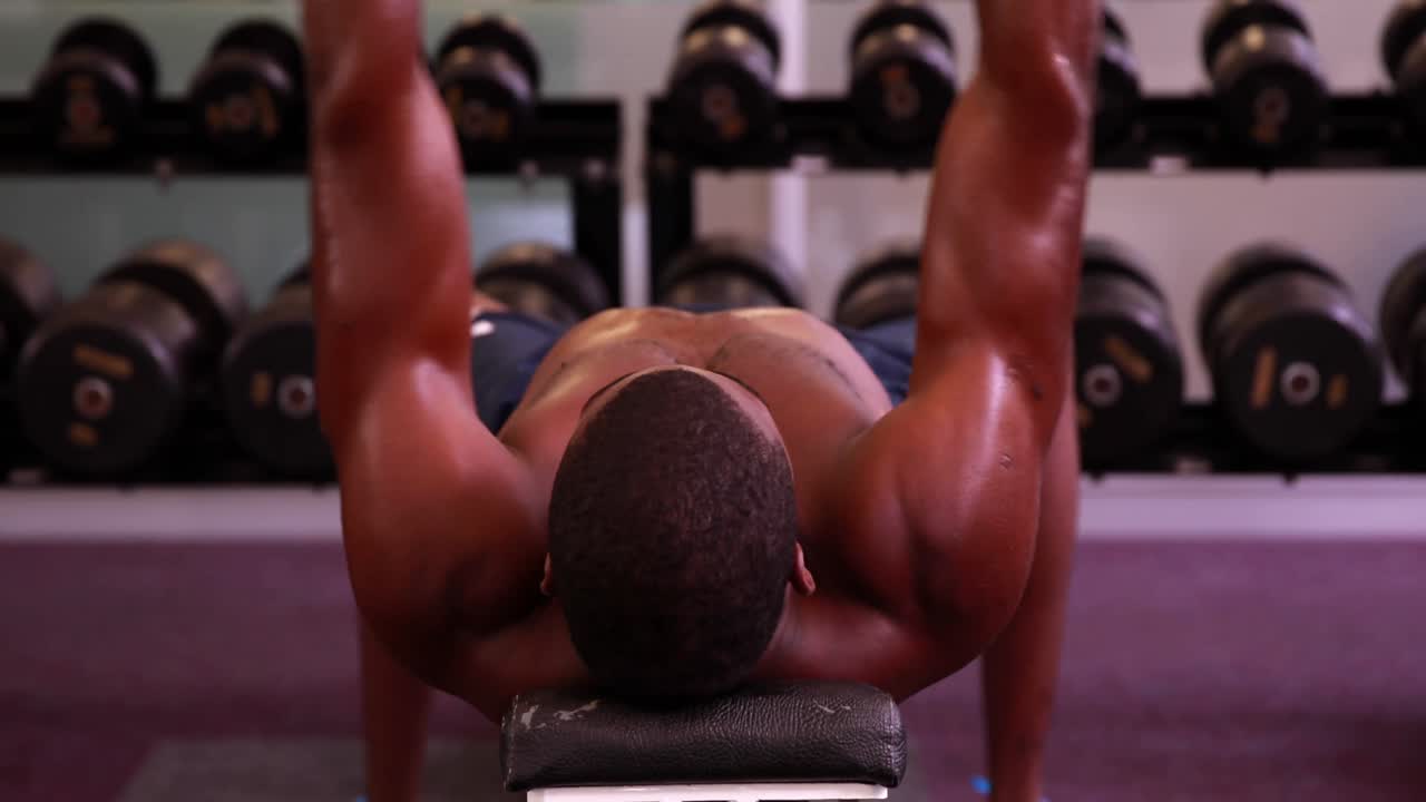 hombre sin camisa levantando pesas acostado en un banco