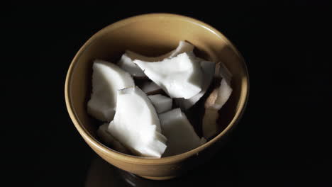 Coconut-pieces-in-a-rustic-bowl-on-black-table-with-a-reveal-movement-from-left-to-right