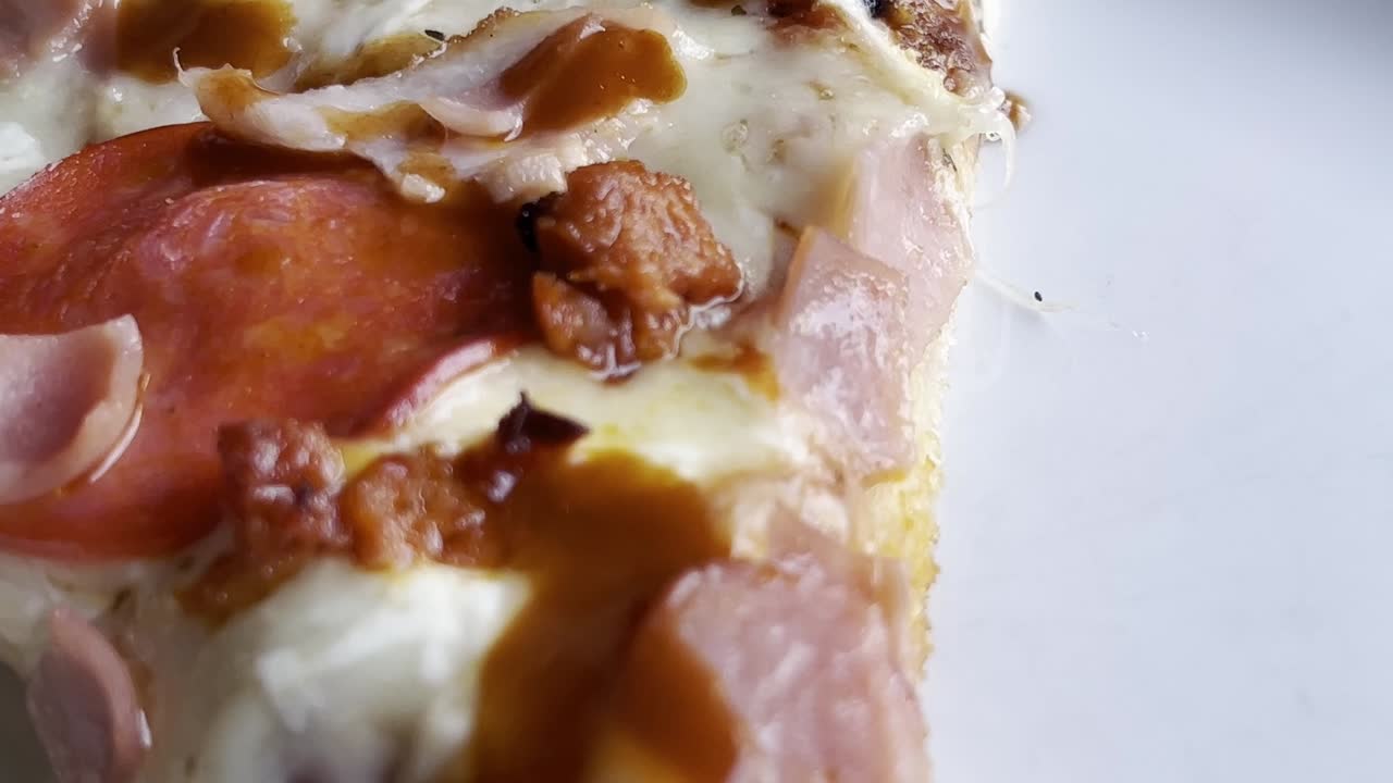 Close-up of a pizza slice topped with pepperoni, ham, melted cheese, and sauce on a white plate