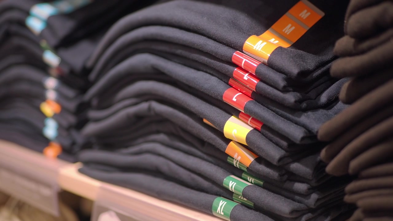 Stacks of Black T-Shirts with Colorful Size Tags on a Store Shelf