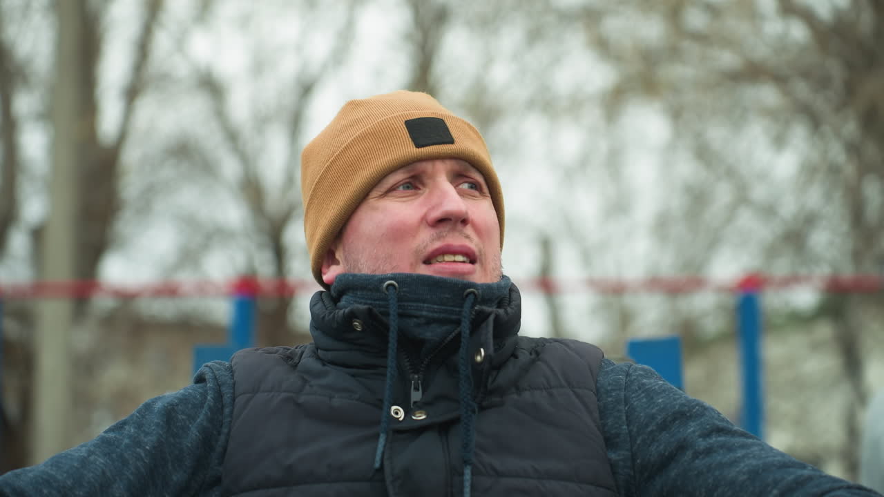 A coach seated on workout equipment appears contemplative, in the background, two boys play football