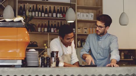 imágenes de video de 4k de un joven guapo de pie con su camarero en el café y usando una tableta digital