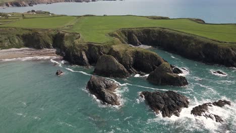 drone shot of waves hitting into rocks on a small headland in ireland on a summer's day