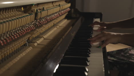 woman playing upright piano with open sound board showing hammers striking the strings