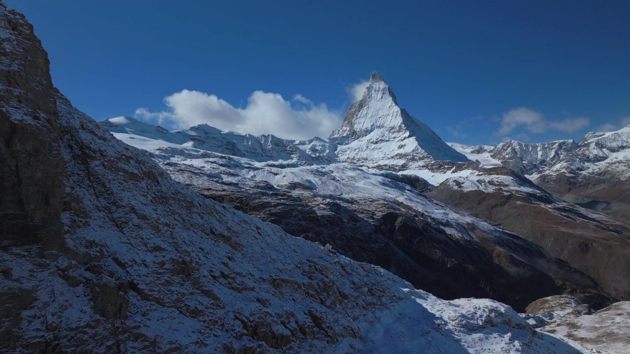 スイスアルプスのツェルマット、マッターホルンの有名な山頂と岩だらけの崖、リッフェルゼー湖。秋から冬にかけての初冠雪、青空の朝。ゴルナーグラート鉄道がゆっくりと上昇するドローン空撮。