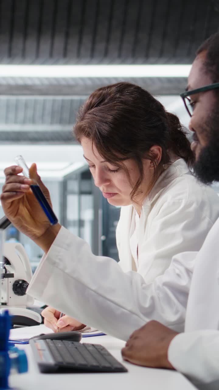 Vertical video Lab chemists inspect liquids in test tube, looking for breakthroughs
