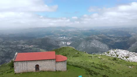 Cows-Grazing-at-the-Edge-of-Monsacro-Mountain-Chapel,-Asturias-Aerial-Landscape-Drone-Panoramic-Shot