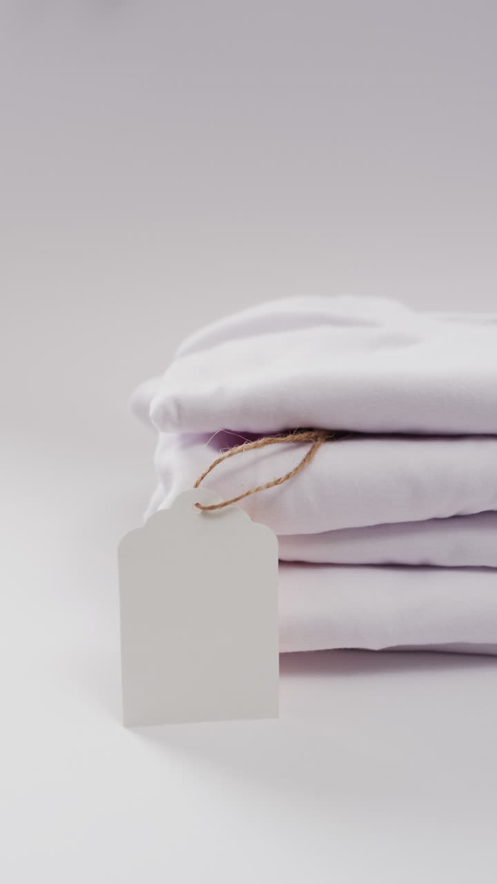 Vertical video of stack of folded white t shirts with copy space on white background