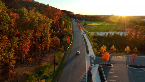 aerial tracking shot of vehicle driving on straight road during autumn fall foliage season sunset