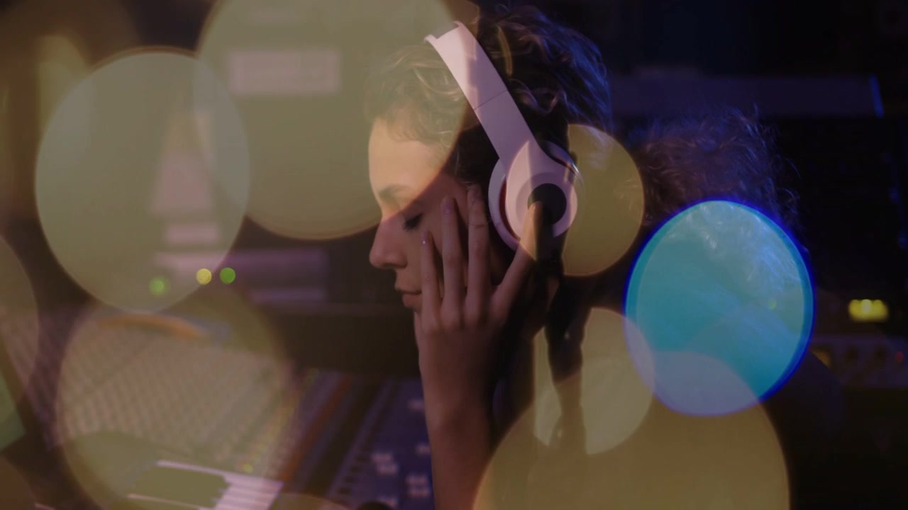 Music producer adjusting headphones, initiating playback and monitoring console with bokeh lights