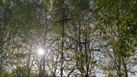 sparkling sun behind à metal cross in a wooded cemetary