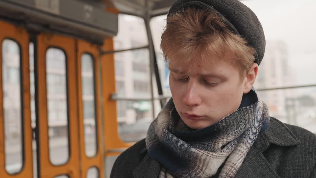 Nachdenklicher Stadtpoet. Kontemplativer junger Künstler, der die städtische Szenerie erkundet. Einsamer Poet, der die graue Stadt vom Fenster aus beobachtet. Einsamer junger Schriftsteller, der das Stadtleben durch den Fensterblick betrachtet.