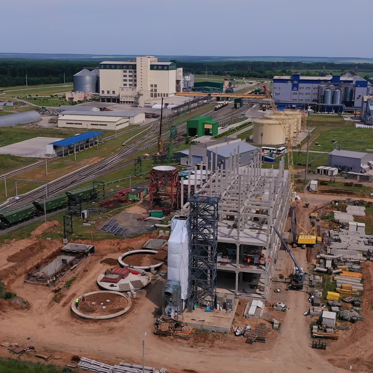 Construction site at the territory of granary plant. New premises construction for future part of the industrial complex. Green fields and forests at the background