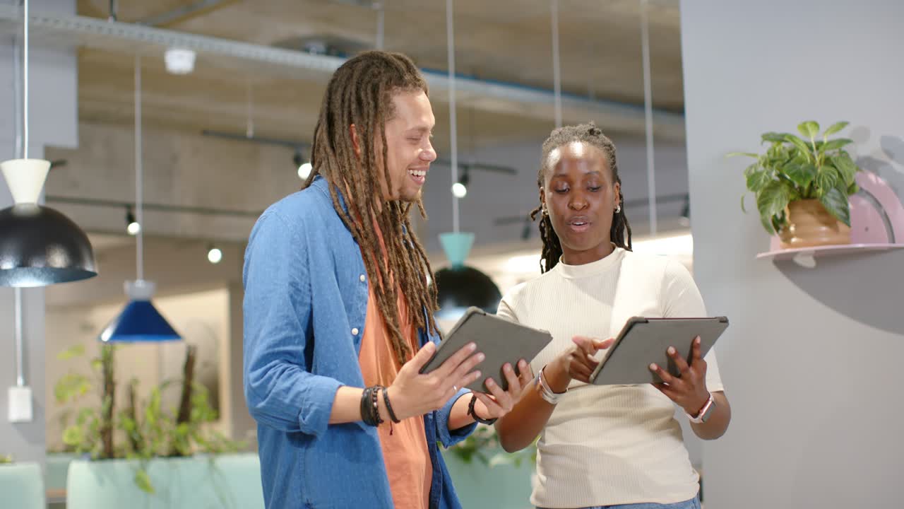 African American coworkers holding tablets at office, comparing content after one rotating tablet