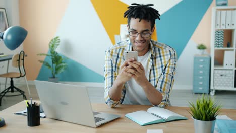 slow motion of cheerful african american guy enjoying smartphone activities in workplace