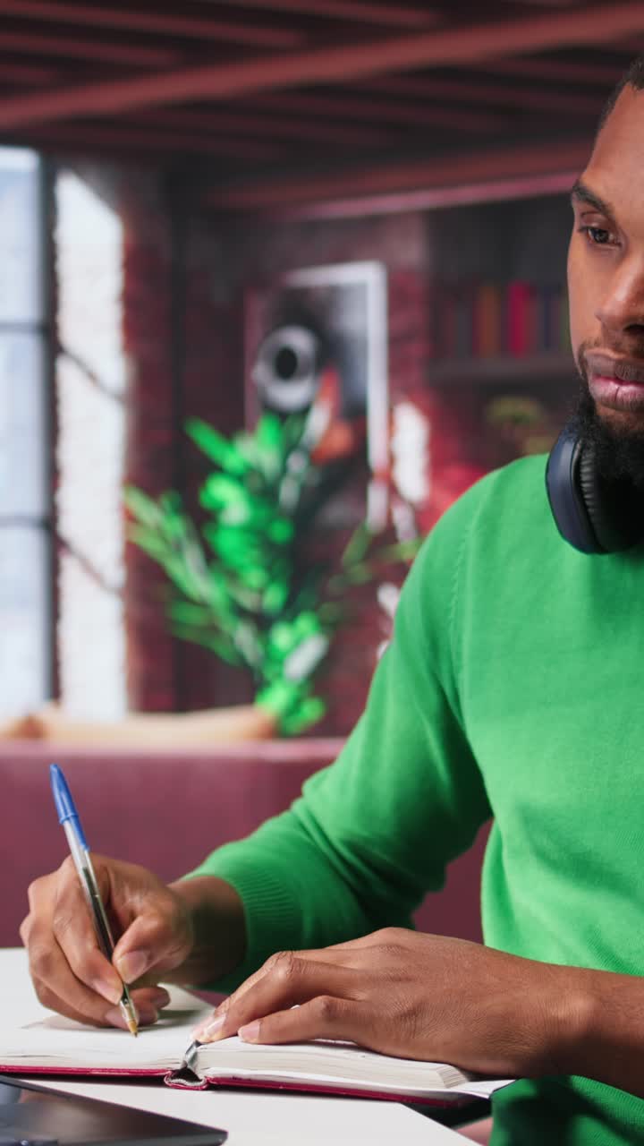 Vertical Video Smiling black man taking notes while watching a tutorial presentation