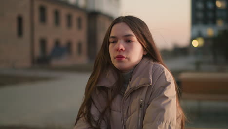 un primer plano de una mujer joven con una chaqueta de melocotón, capturada con una expresión de dolor en su rostro. el fondo está suavemente borroso