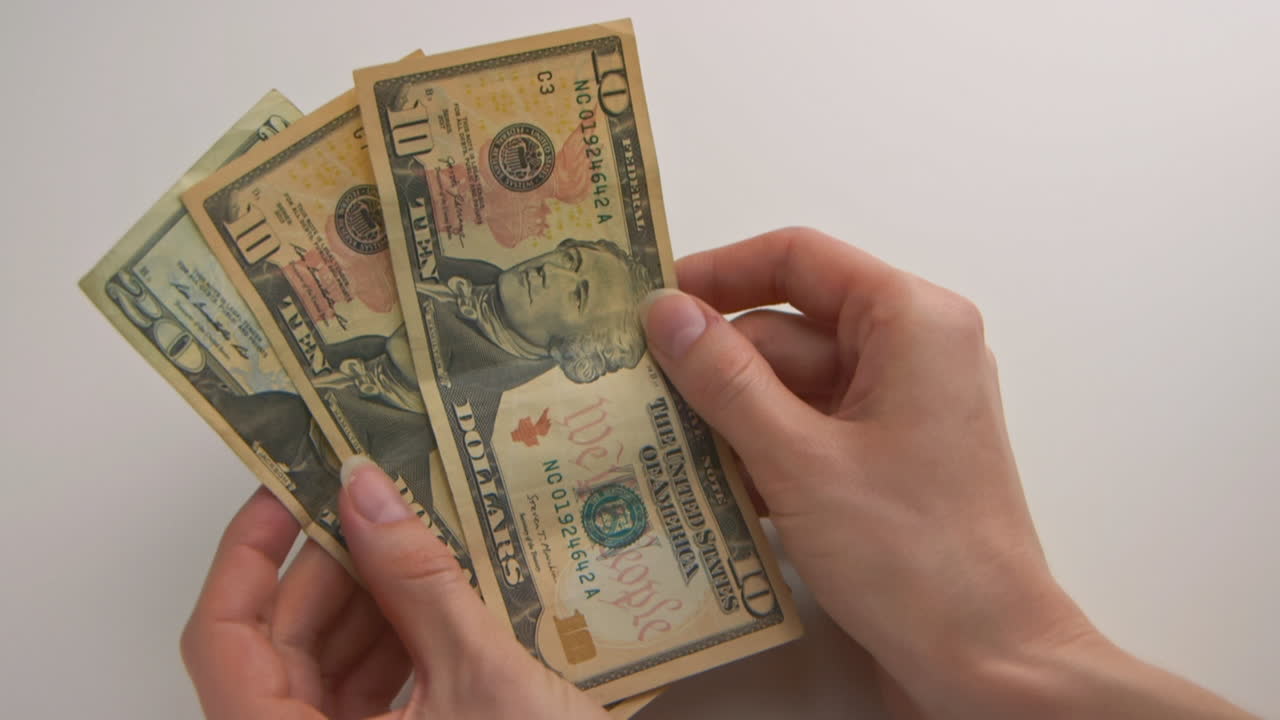 A caucasian woman's hands counts American money and places the bills on the table