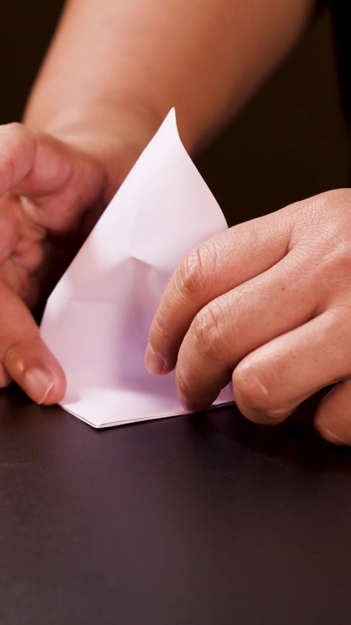 Adult hands carefully fold white paper into an origami boat under soft, warm lighting