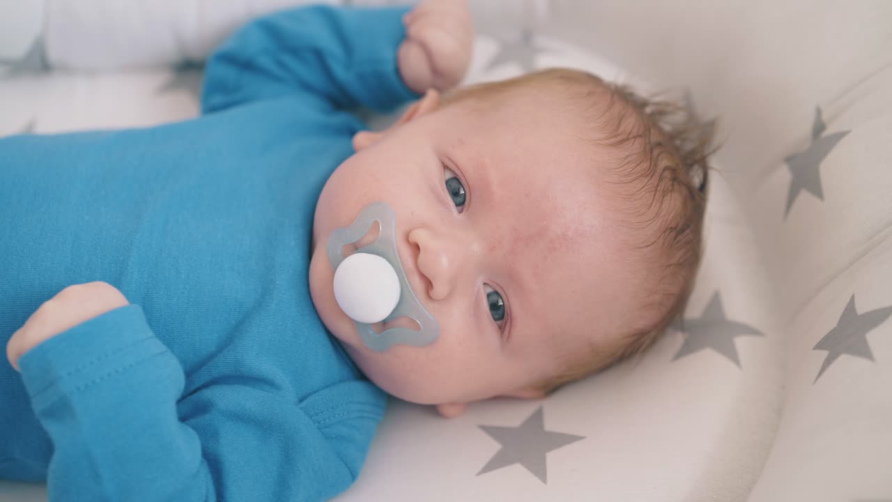 Glad nyfödd bebis suger på napp i kokong i en vagga