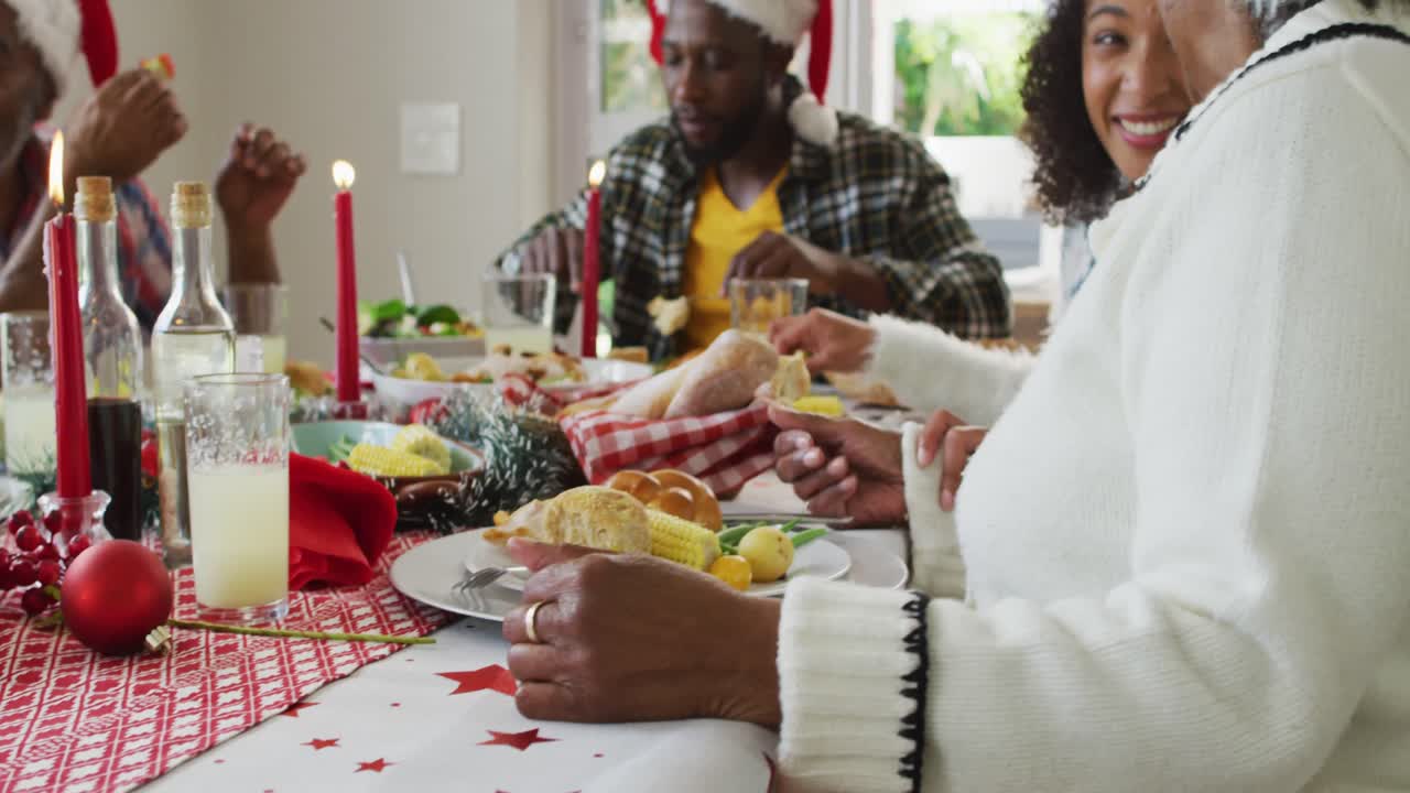feliz familia afroamericana de varias generaciones con sombreros de papá noel y celebrando la comida navideña