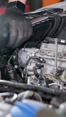 a person's gloved hand working on a car engine with a flashlight